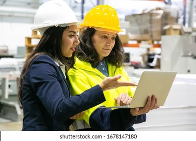 Confident Female Workers With Laptop At Manufacturing Plant. Two Female Employees Talking While Standing At Factory With Laptop. Print Manufacturing Concept