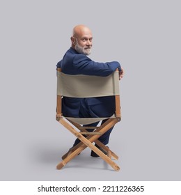 Confident film director sitting on the director's chair and looking at camera: video production, filmmaking and film industry concept