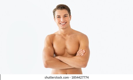 Confident Fit Man. Portrait of attractive muscular man with naked torso and smooth skin standing with crossed arms, isolated over white background. Shirtless guy posing at studio, looking at camera