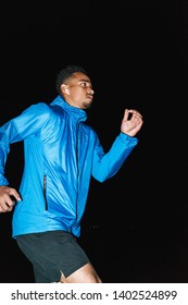 Confident Fit Young African Sports Man Wearing Windbreaker Exercising Outdoors At Night Time, Running At The Beach