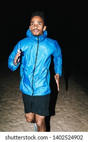 Confident Fit Young African Sports Man Wearing Windbreaker Exercising Outdoors At Night Time, Running At The Beach