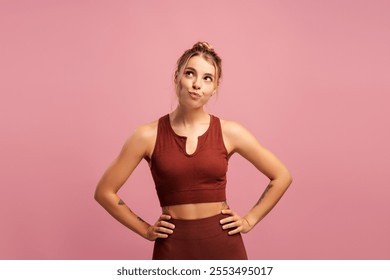 Confident fit young woman posing, looking up, holding hands on hips, isolated on pink background. Sport, health care, wellness concept - Powered by Shutterstock