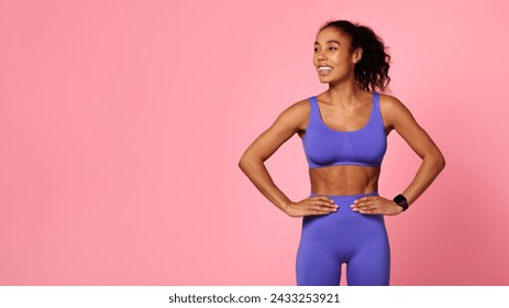 Confident fitness model. Athletic African American woman in purple sportswear stands with hands on hips, looking aside, showcasing strength and wellness on pink backdrop, panorama with copy space - Powered by Shutterstock