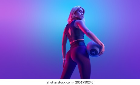 Confident fitness woman posing with a medicine ball. Attractive blonde sportswoman portrait holding with medicine fitness ball neon style creative light. - Shutterstock ID 2051930243