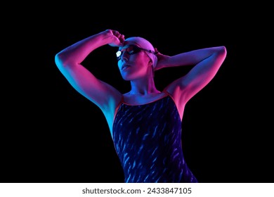 Confident, focused on competition young swimmer in swimming uniform posing in vibrant neon light against black studio background. Concept of professional sport, motion, strength and power. Ad - Powered by Shutterstock