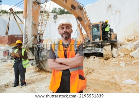 Confident foreman in reflective vest and safety helmet looking at camera while standing on construction site against truck Foto stock © 