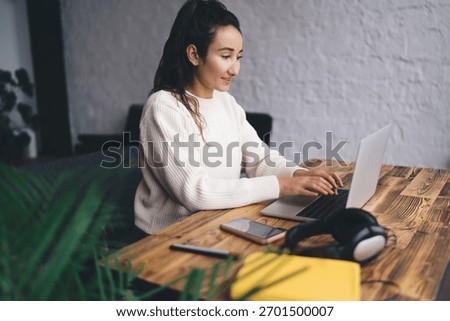 Confident freelancer smiling at laptop while typing, immersed in digital workflow, showing ease with technology and mastery of flexible modern working culture and virtual presence.