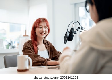 A confident and friendly Asian female podcaster is enjoying a conversation as she interviews a guest in her studio, recording a podcast with a special guest. - Powered by Shutterstock