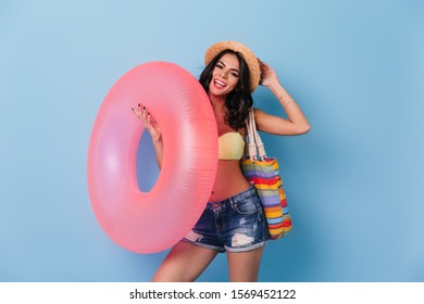 Confident girl holding pink swimming circle. Front view of amazing tanned lady isolated on blue background.