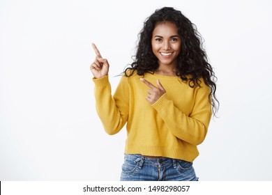 Confident good-looking african-american girl with curly hairstyle, look camera self-assured and sassy smiling, pointing upper left corner, introduce amazing product, give recommendations