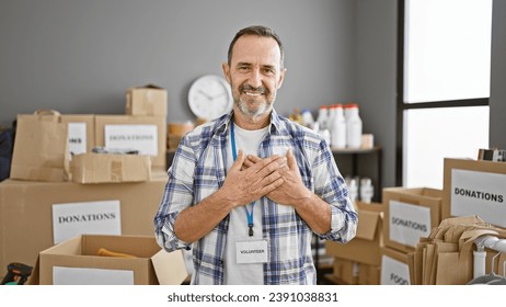 Confident grey-haired middle-aged man standing with heart filled hands, smiling as a volunteer in his community charity center - Powered by Shutterstock