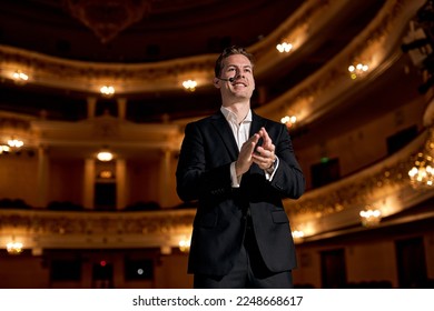 Confident guy of american appearance in formal classic suit clapping hands after performance, giving speech, on stage. Presenter Speaking to Audience People. Unidentifiable Audience and Presenter. - Powered by Shutterstock