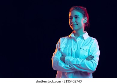 Confident. Half-length Portrait Of Young Pretty Girl In White Shirt Isolated On Dark Background In Blue Neon Glow. Concept Of Emotions, Facial Expression, Youth, Aspiration, Sales. Copy Space For Ad