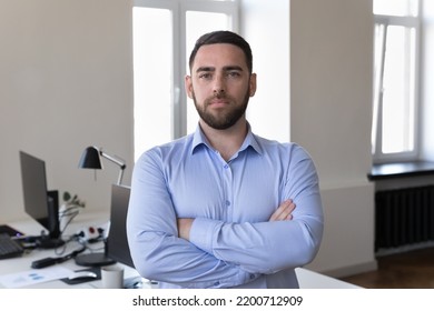 Confident Handsome Caucasian Business Leader Man Head Shot Portrait. Serious Businessman, Executive, Entrepreneur Looking At Camera With Arms Folded, Standing At Office Work Table