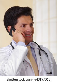 Confident Handsome Doctor With An Stethoscope Around His Neck, Using A Celphone With One Hand, In Office Background