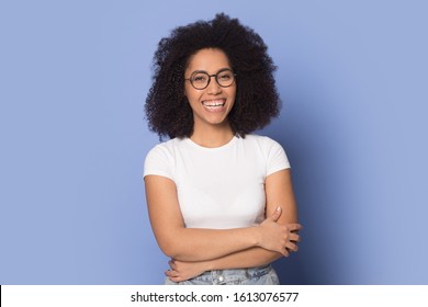 Confident happy african american young woman wearing spectacles, standing with folded hands head shot portrait. Smiling female client satisfied with optic clinic service isolated on blue background.
