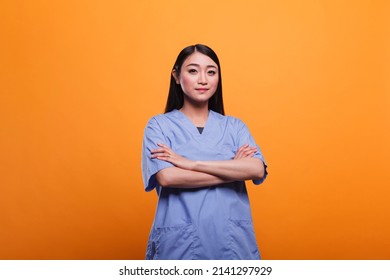 Confident And Happy Asian Hospital Staff Worker With Hands In Pockets, Wearing Clinic Related Clothing. Portrait Of Attractive Smiling Nurse Wearing Blue Medical Uniform While Looking At Camera.