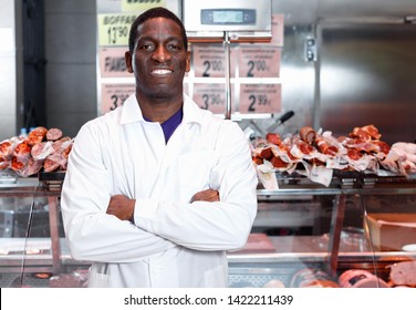 Confident happy cheerful  male owner of butcher shop standing with arms crossed in front of counter with meat products - Powered by Shutterstock