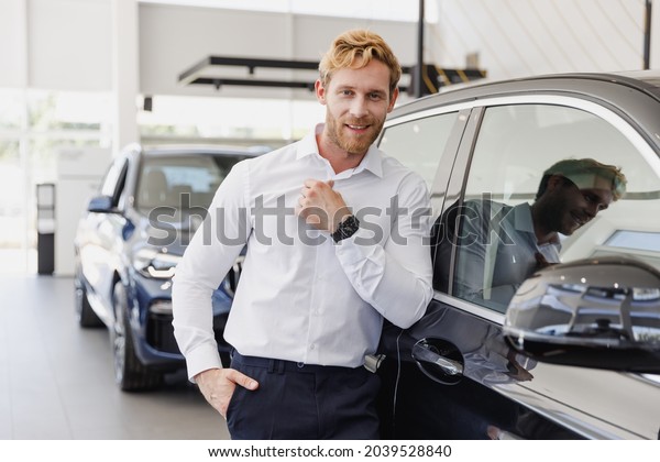 Confident happy man customer buyer businessman\
client wears white shirt chooses auto wants to buy new automobile\
in car showroom vehicle salon dealership store motor show indoor.\
Car row sales concept