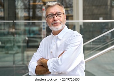 Confident happy mature older business man leader, smiling middle aged senior old professional businessman wearing white shirt glasses crossed arms looking at camera standing outside, portrait. - Shutterstock ID 2249718653