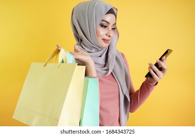 confident happy muslim woman shopping online and order the product through mobile application. Islamic customer woman hand holding shopping bag isolated over blue background.  Technology concept.