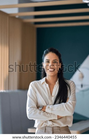Confident happy professional young latin business woman company employee, lady executive manager, smiling female worker or entrepreneur looking at camera standing in modern office, vertical portrait.