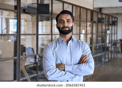 Confident happy successful ceo financial manager. Bearded indian businessman looking at camera standing in modern office with arms crossed. Handsome classy corporation owner. Business portrait.