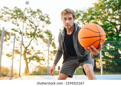 Confident Happy Sunlit Young Sporty Sportsman Man 20s In Grey Sports Clothes Training Look Camera Holding In Hand Giving Ball Play At Basketball Game Playground Court. Outdoor Courtyard Sport Concept