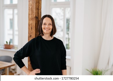 Confident Happy Woman With A Vivacious Smile Standing In A High Key Living Room With Hand On Hip Grinning At The Camera