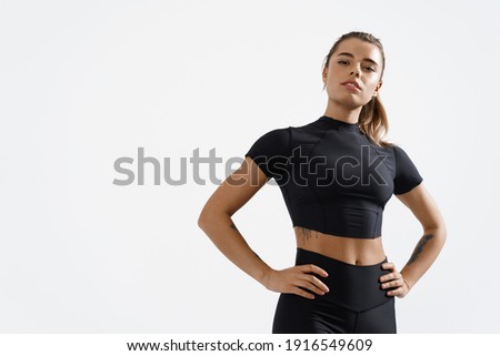 Confident healthy and athletic woman staring determined at camera, holding hands on hips. Sportswoman exercising in sport clothing, training and workout on white background.