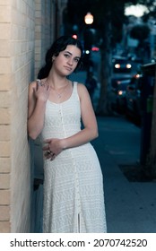 Confident High School Senior Girl Leaning Against Contemporary Brick As Dusk Settles Over The Downtown Area Of Ventura.