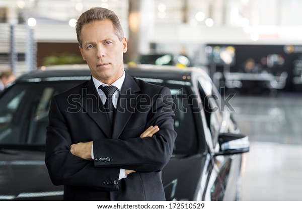 Confident in his choice.\
Mature grey hair man in formalwear standing in front of car and\
looking at camera