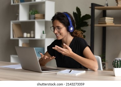 Confident Hispanic Female Interpreter Work From Home Office Sit At Desk In Headset Talk Look On Laptop Screen Translate Online Event. Young Lady Participate At Web Conference Negotiate Using Pc Webcam