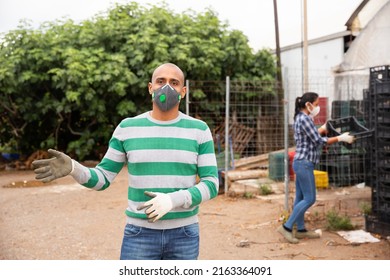 Confident Hispanic Man Farm Worker In Protective Face Mask Standing Outside Near Greenhouse Buildings