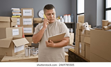 Confident hispanic young man standing at charity center, volunteering his service, reading donation documents while smiling and having a warm conversation on his smartphone - Powered by Shutterstock