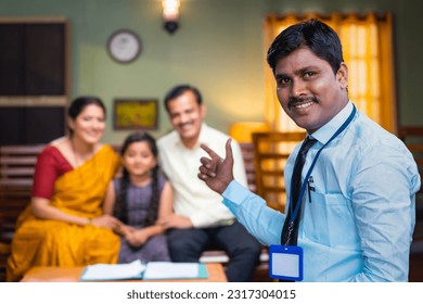 Confident indian banker pointing finger by looking camera in front on happy family at home - concept of expert advice, financial doorstep services and insurance policy agent