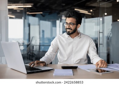 Confident Indian man with a beard, in shirt, programming on laptop at office desk. Exuding positivity and professionalism in a business environment. - Powered by Shutterstock