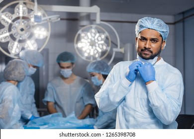 Confident Indian surgeon looking at camera in surgical room hospital, medical doctor wear green surgery scrub suit.