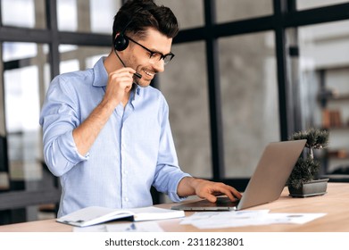 Confident intelligent caucasian man, wearing glasses and headset, office or call center employee, standing near workplace in office, communicating with colleagues or client by online conference - Shutterstock ID 2311823801