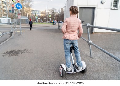 Confident Kid Girl Stand And Ride Near Road On Modern Eco-friendly Electric Self-balancing Scooter. Electric Hoverboard On City Street.