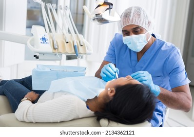 Confident Latin American Stomatologist Treating Teeth Of Female Patient In Modern Dental Office