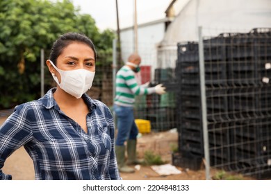 Confident Latino Woman Farm Worker In Protective Face Mask Standing Outside Near Greenhouse Buildings