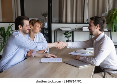 Confident Lawyer Meeting And Shaking Hands With Happy Couple Of Clients. Husband And Wife Visiting Office Of Mortgage Broker, Real Estate Agent, House Seller Shaking Hands Over Signed Contract