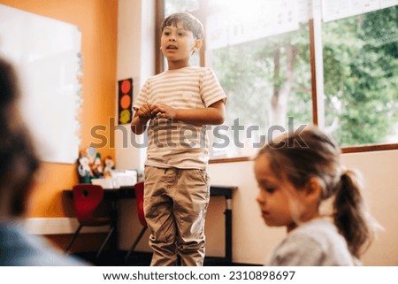 Confident little boy stands in front of his class to give a speech in a language class. Male elementary school pupil develops his public speaking skills during an oral lesson.