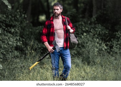 Confident lumberjack works in summer forest. Man with an ax. Woodcutter in plaid shirt in forest. Hipster with axe. Lumberjack with an axe. Bearded lumberjack. American lumberjack with hatchet.