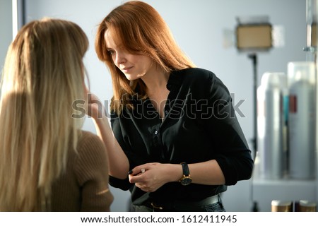 confident make-up artist with beautiful young caucasian girl client in beauty saloon, using brushes and different decorative cosmetics