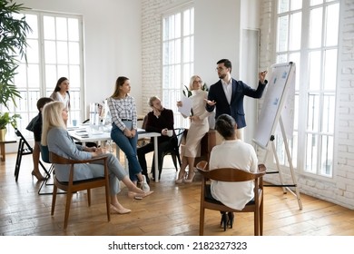Confident male boss or trainer make whiteboard presentation for diverse employee at team office meeting. Businessman talk lead briefing, present project on flip chart at team training or briefing. - Shutterstock ID 2182327323