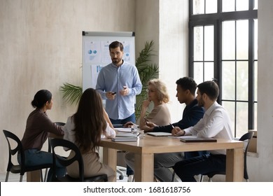Confident male Caucasian team leader head meeting in office, present project on whiteboard, man speaker or coach talk make flip chart presentation to multiracial colleagues at briefing