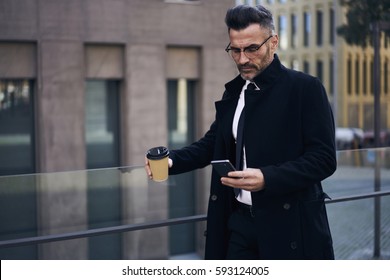 Confident male CEO supervising work of employees checking financial reports in online database via smartphone connected to fast 4G internet during work break standing outdoors with cup of coffee - Powered by Shutterstock