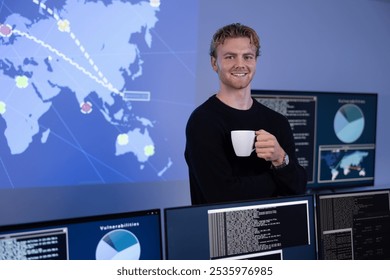 Confident male Cybersecurity Analyst with coffee cup in large Cyber Security Operation Center SOC handling Threats